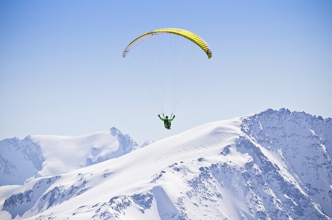 Person paragliding over snowy mountain