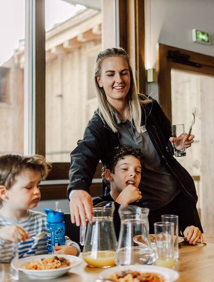 Smiling VIP SKI nanny serving lunch to young children in childcare