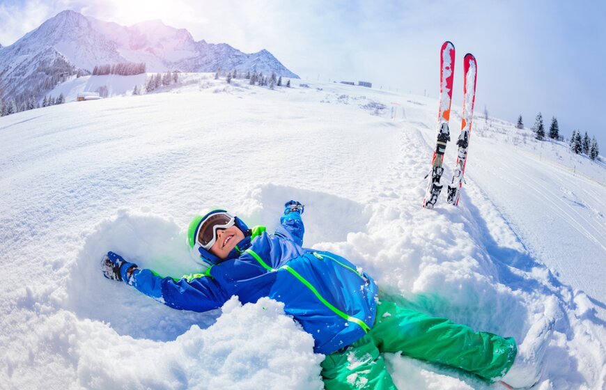 Boy doing snow angel in powder snow on side of piste
