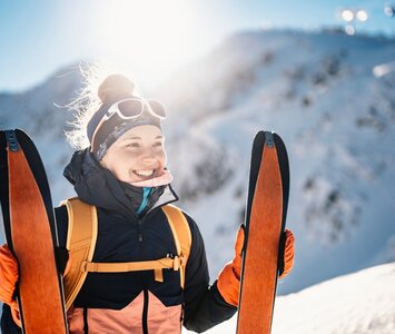 Female skier standing with ski touring skis at top of mountain
