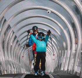 Child coming up magic carpet ski lift with poles in the air