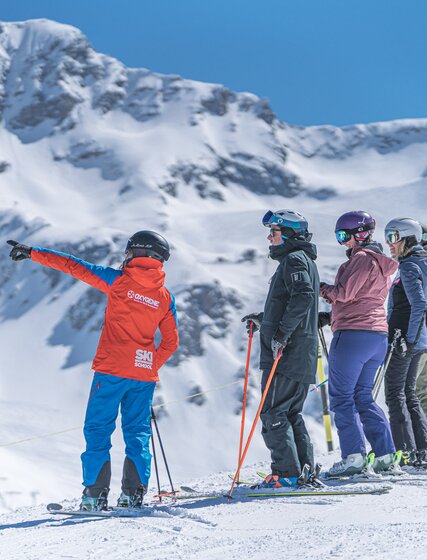 Oxygene ski instructor pointing at mountain wiht group of skiers