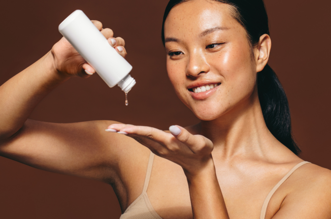 Smiling woman pouring skincare product out of bottle onto hand