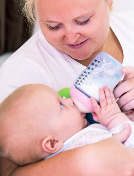 Nanny giving young baby bottle of milk