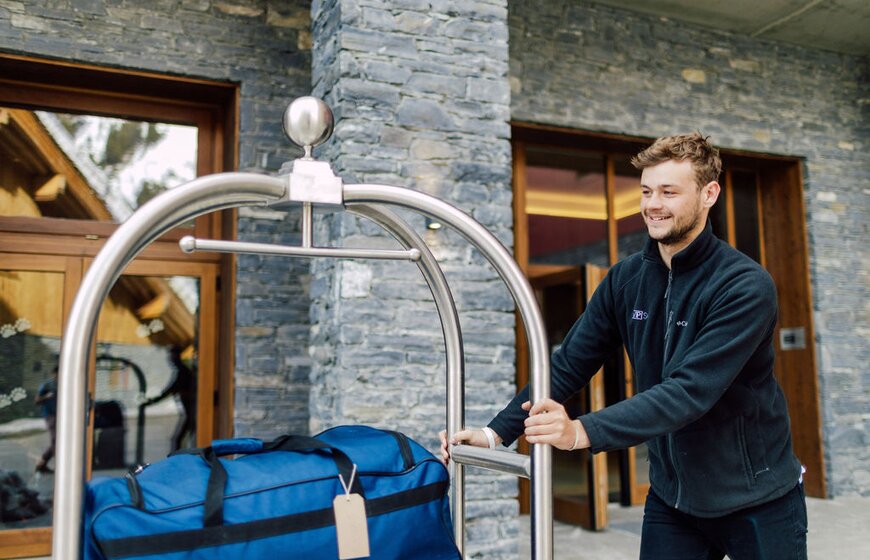 Young man pushing luggage trolly outside ski hotel