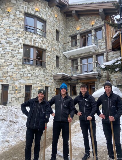 Four smiling VIP SKI staff members holding snow clearing shovels
