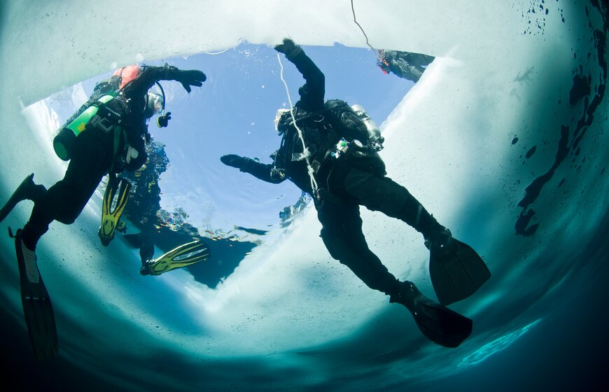 Two people ice diving beneath hole in the ice