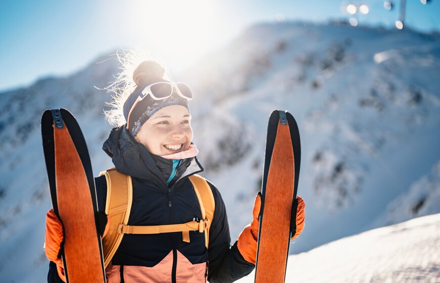 Smiling female skier holding up touring skis with skins on