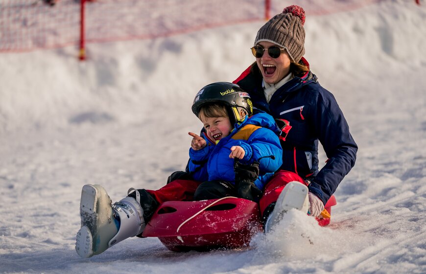 Smiling woman sledging with young son