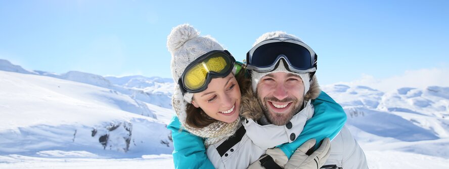 Couple smiling, wearing ski goggles on the piste