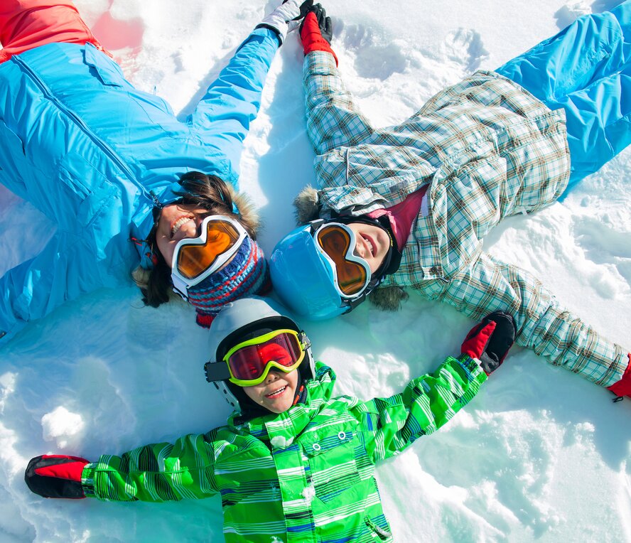 family laying in the snow with ski goggles
