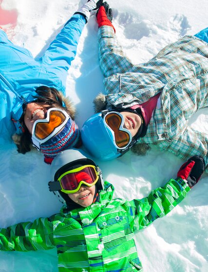 Mother and two children in ski gear lying down on snow looking up at camera