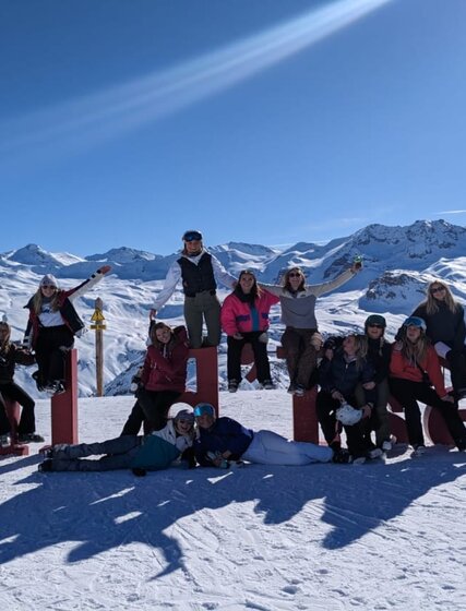 Smiling VIP SKI seasonnaires sitting on Val d'Isere letters