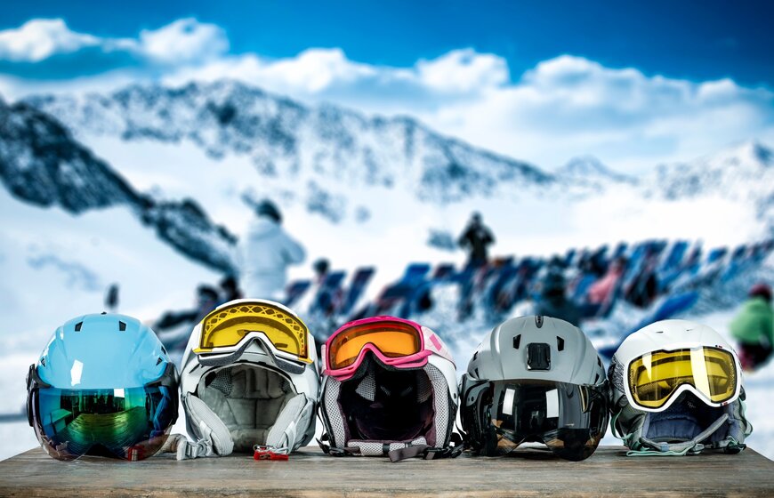 Five ski helmets with goggles lined up on a table at mountain restaurant