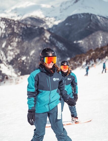 Two smiling young women on snowboards on the piste