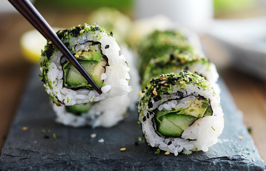 Vegetarian sushi on a slate plate being lifted up by chopsticks