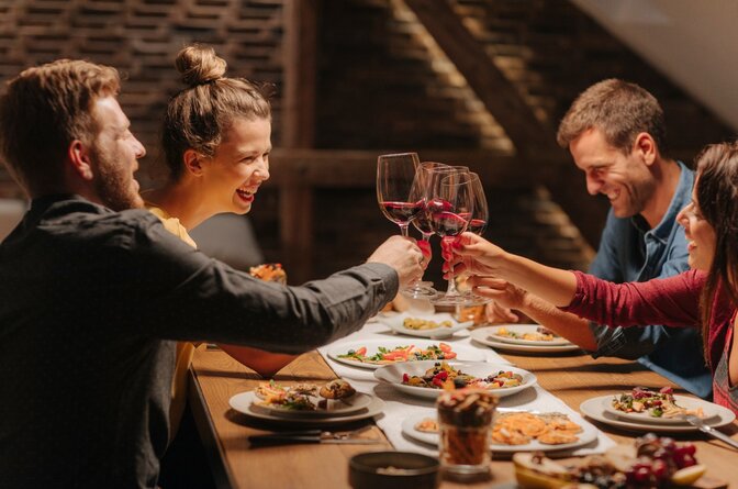 Two smiling couples clinking glasses of red wine together over table of food