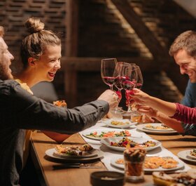 Two smiling couples clinking glasses of red wine together over table of food