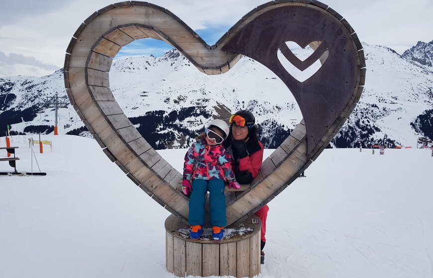 Ski Mindset Coach Kate Casali and daughter posing for ski photo in wooden heart on the ski slopes