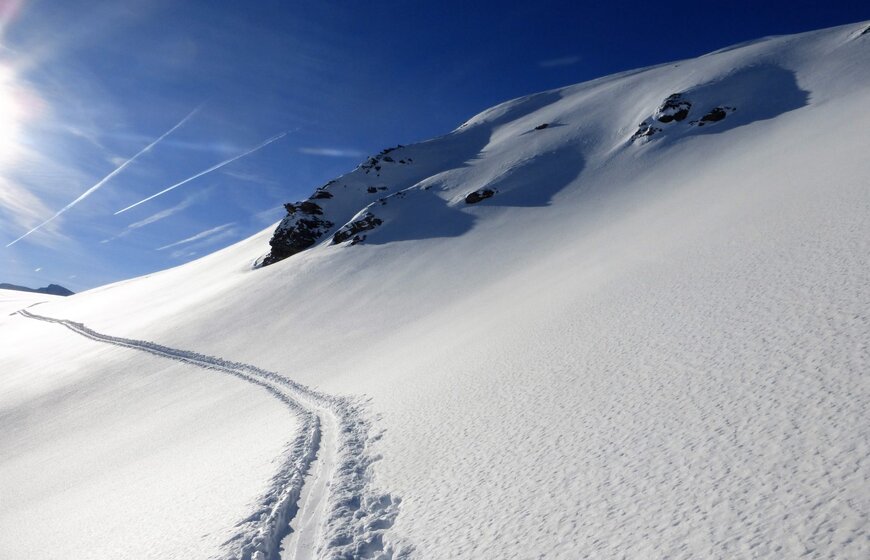 Fresh ski touring tracks on side of ski mountain on blue sky day