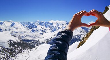 Person making heart shape with hands at the top of the mountain looking down the valley on a sunny day