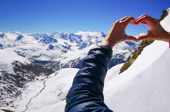 Person making heart shape with hands at the top of the mountain looking down the valley on a sunny day
