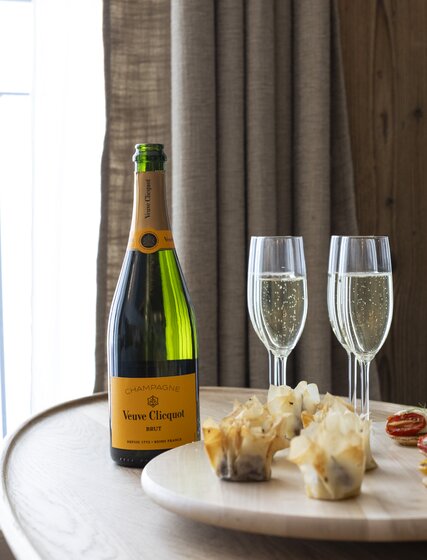 Bottle of Veuve Clicquot champagne and two types of canapés on a wooden board 