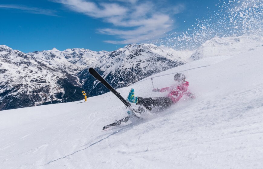 Female skier falling down ski slope with skis that have come off