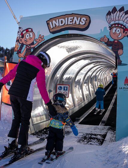 Mother helping young child onto magic carpet ski lift in La Plagne