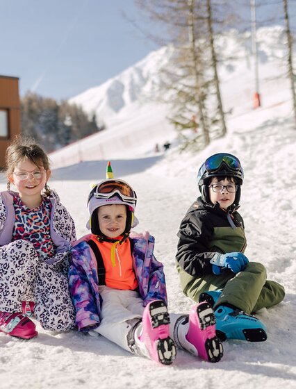 Three children sitting on snowy slope in ski boots