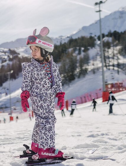 Young girl in ski kit looking behind her on the slopes