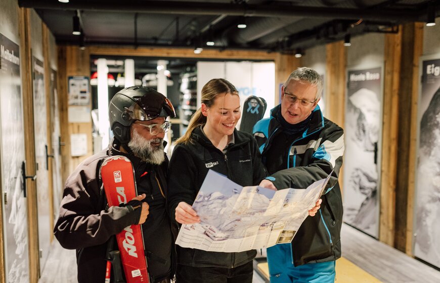 Two male skiers with chalet host in ski room in the Graciosa looking at piste map