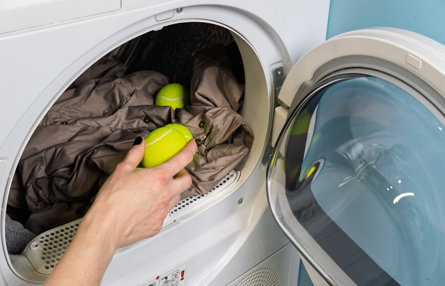 Woman adding tennis balls to tumble dryer with down jacket inside