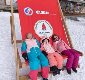 Three smiling children sitting in oversized deckchair in La Plagne