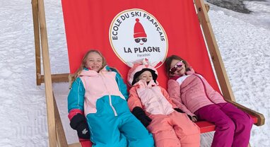 Three smiling children sitting in oversized deckchair in La Plagne