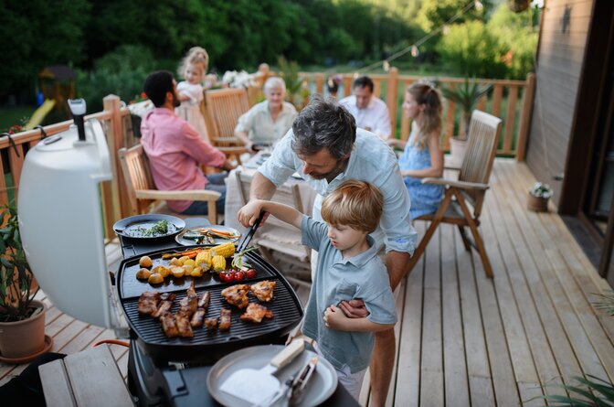 Father helping son take food from BBQ at multigenerational family gathering