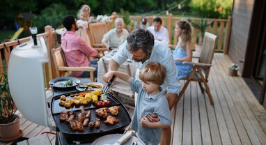 Father helping son take food from BBQ at multigenerational family gathering
