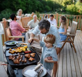 Father helping son take food from BBQ at multigenerational family gathering