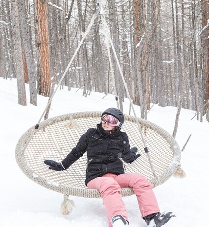 Young person sitting on rope swing in snowy forest
