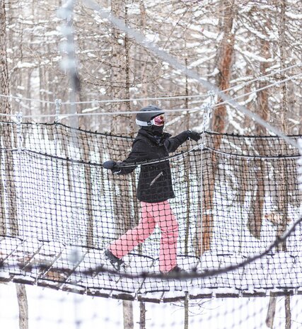 Young person walking along wooden rope path in Val d'Isere forest