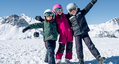 3 smiling children in ski gear on mountain in Val d'Isere