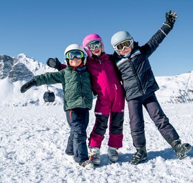 3 smiling children in ski gear on mountain in Val d'Isere