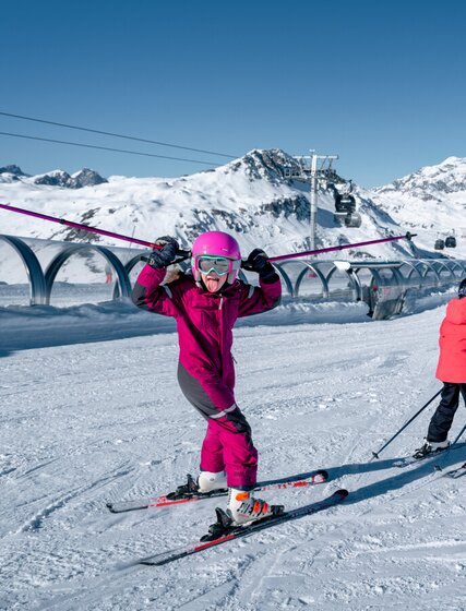 Two young skiers on beginner slope, one with ski poles in the air and tongue out