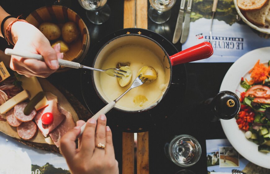 New potatoes being dipped into a cheese fondue with charcuterie and salad on the table