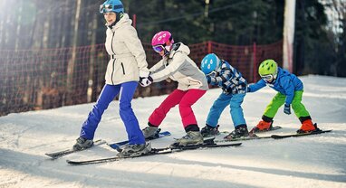 Mum snowploughing down ski slope with 3 children holding on to her