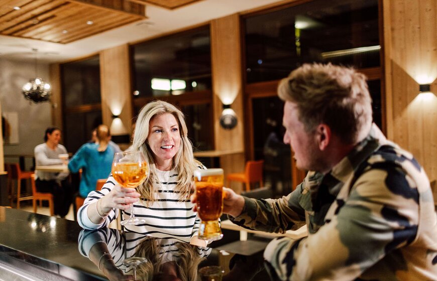 Smiling couple sitting at bar in Bear Lodge raising glass to each other 